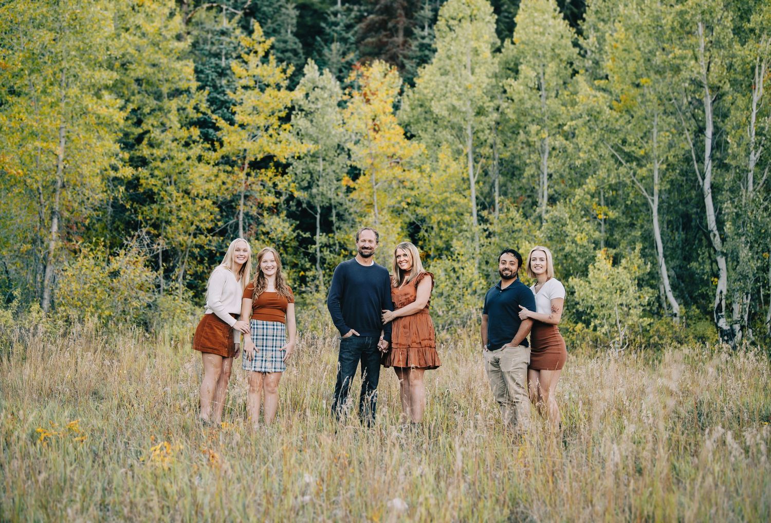 A group poses together in a scenic autumn field with golden aspen trees in the background.