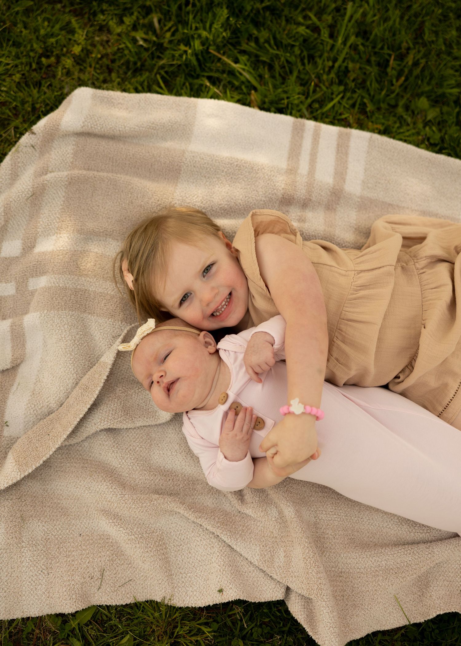 Two young children cuddling and laughing together on a striped blanket outdoors.