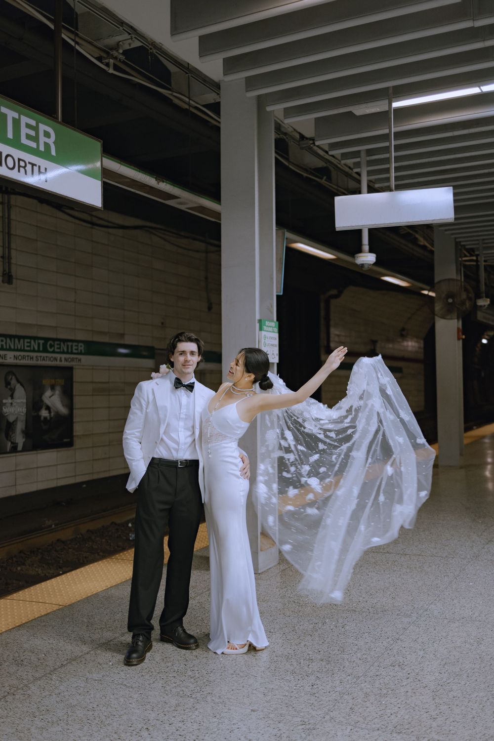 Bride's dress flowing dramatically during photo shoot in subway station.