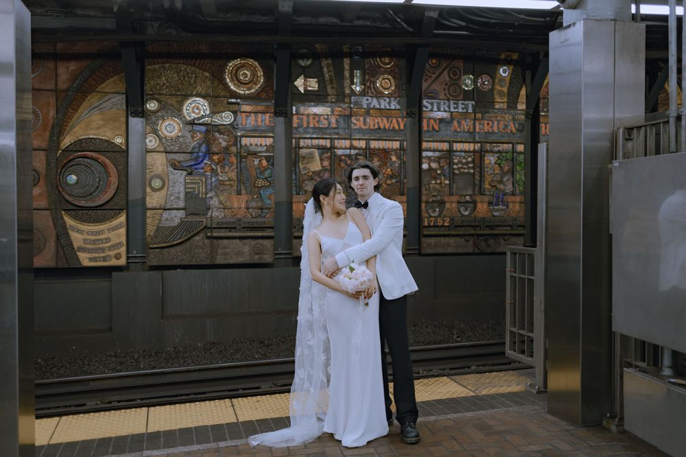 A couple in wedding attire poses together near subway tiles in an urban station environment.