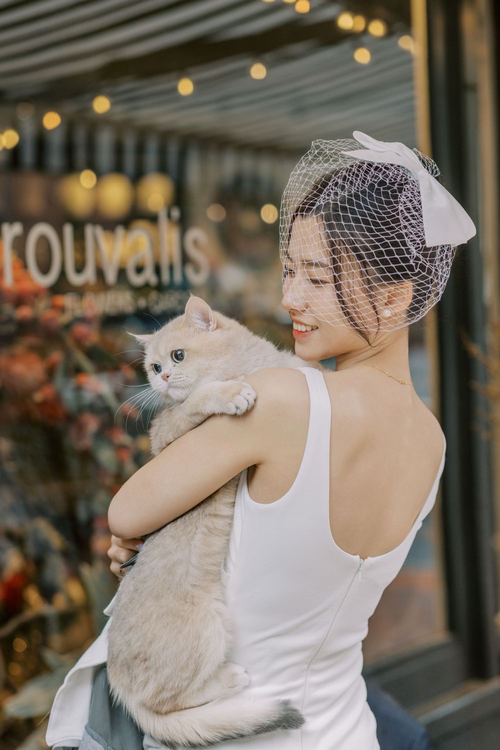 Bride in white dress holding a fluffy cat outside a storefront.