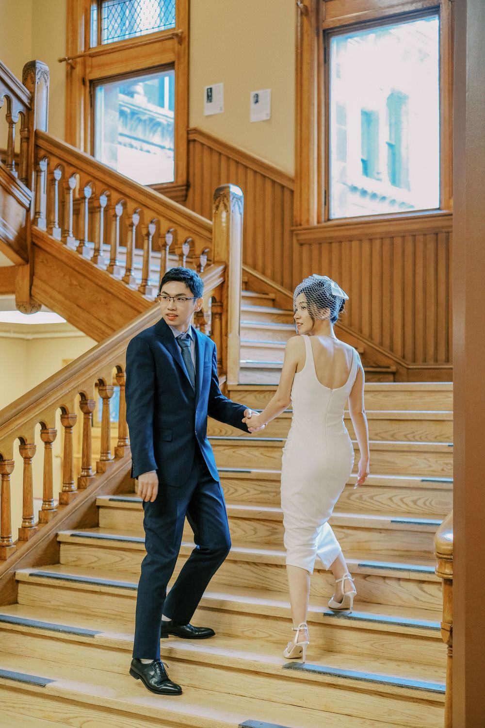 A couple descends wooden stairs inside a historic building with wainscoting.