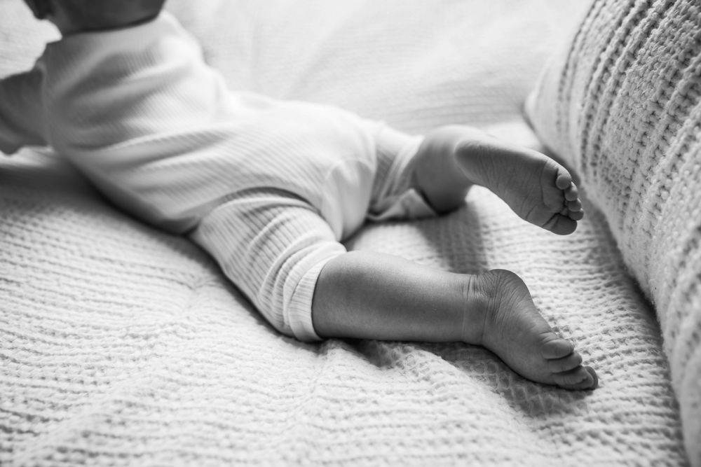 Close-up black and white view of tiny baby feet resting on a textured white blanket.