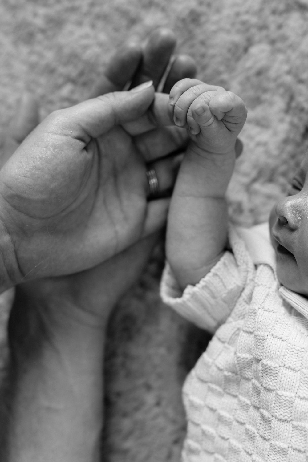 A tender black and white close-up of an adult hand holding a tiny baby's hand and foot.