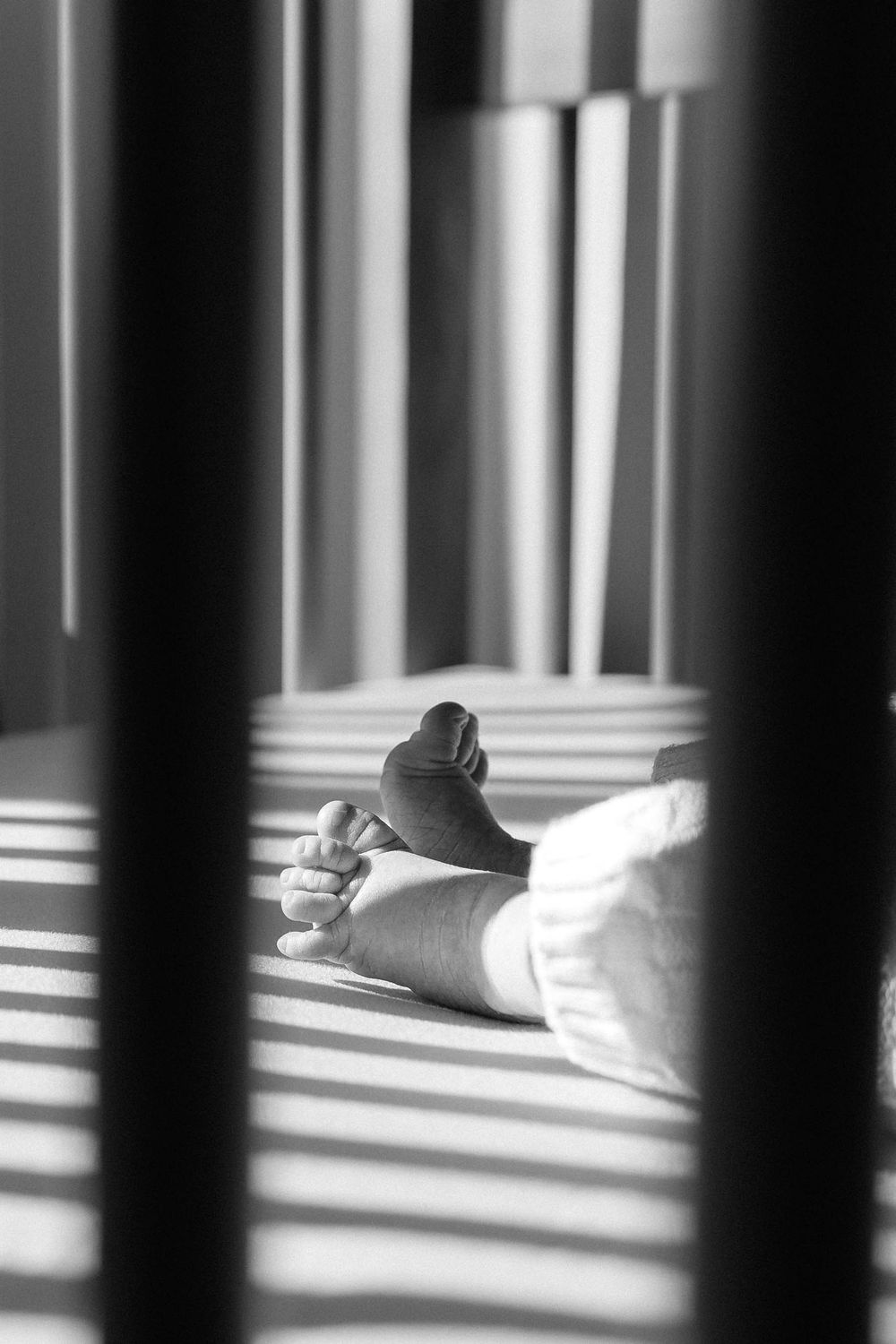 Black and white photograph of light streaming through bars casting shadows on a resting foot in a shoe.