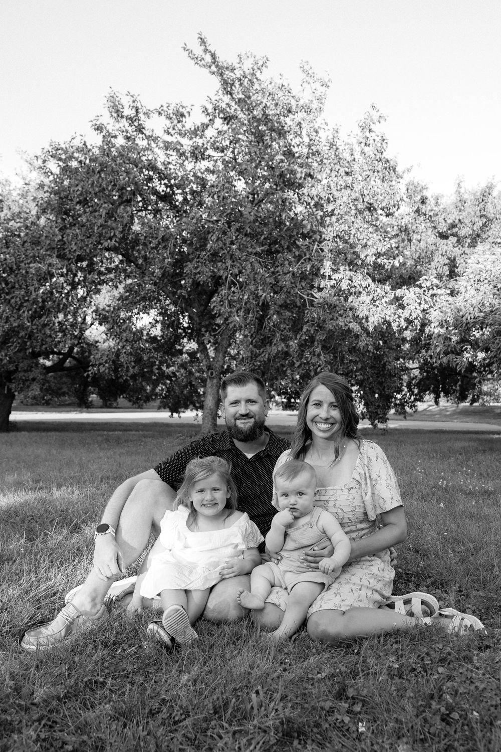 A family relaxes together on grassy hill in black and white photograph.