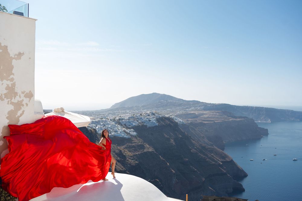 Vibrant red fabric flowing against white buildings and scenic caldera views in Santorini, Greece.
