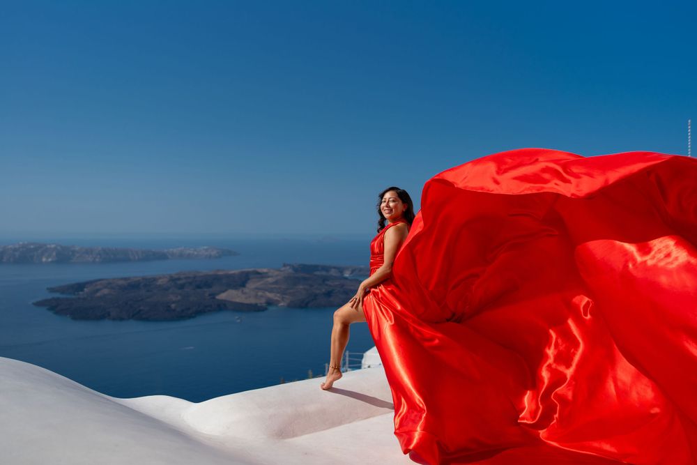 Flowing red dress contrasts against white architecture and blue waters of Santorini.