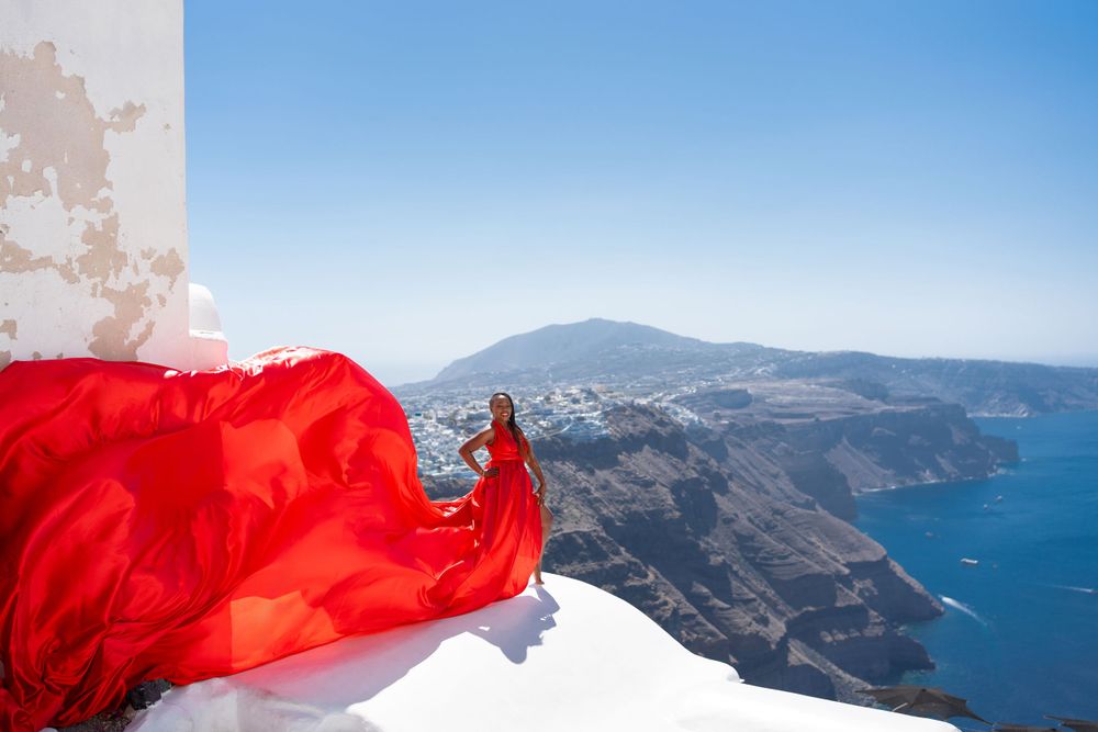 Red fabric flowing dramatically against white buildings overlooking Santorini's caldera.
