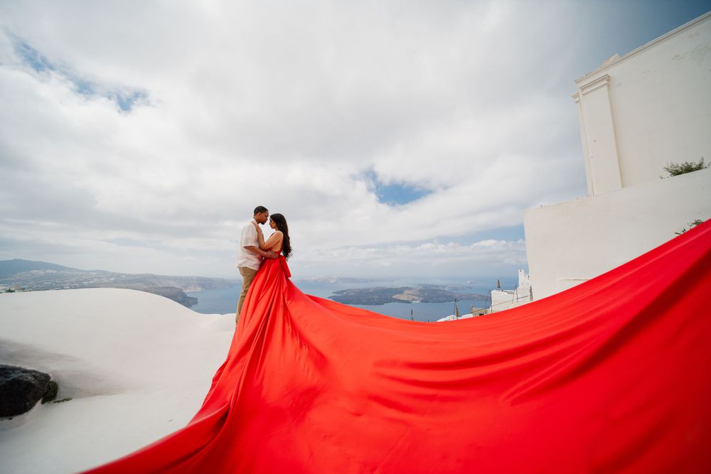 Red flowing gown creates dramatic silhouette against white Cycladic architecture.