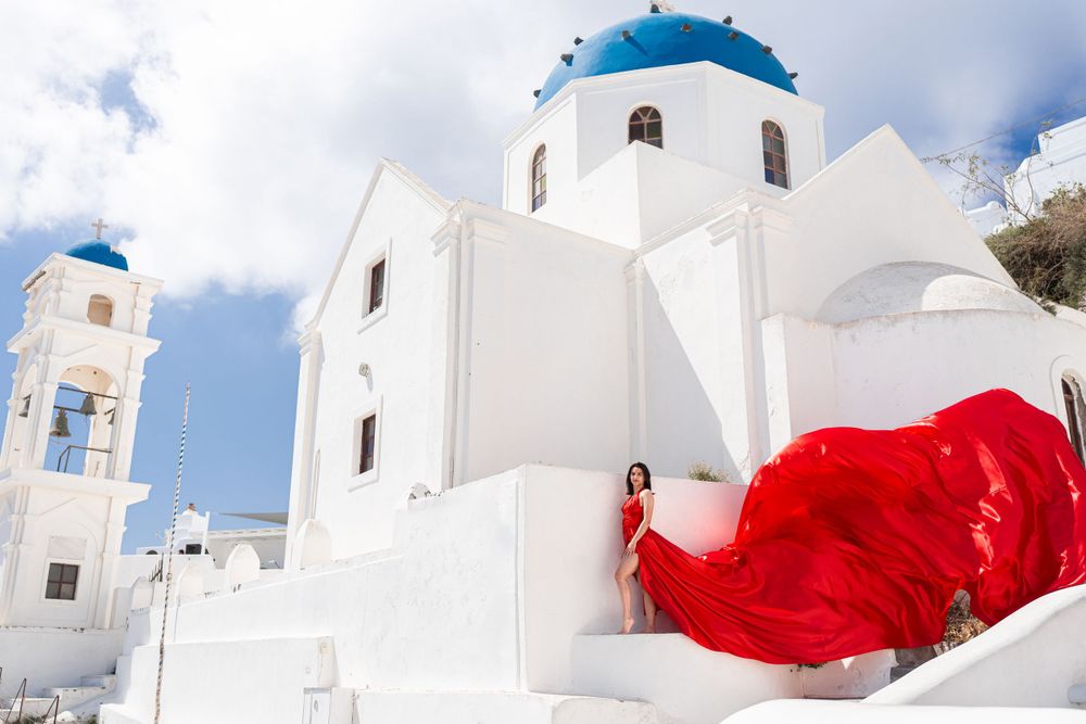 Bright red flowing fabric creates stunning contrast against white church architecture in Santorini.