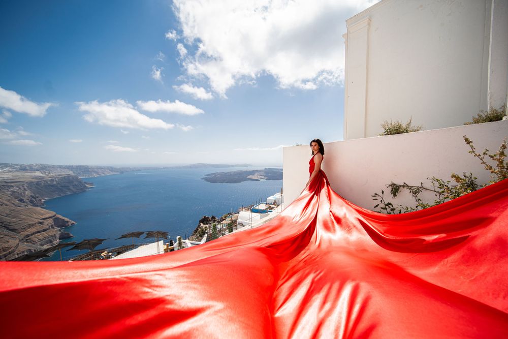Vibrant red flowing fabric spreads dramatically across white buildings with Mediterranean views.