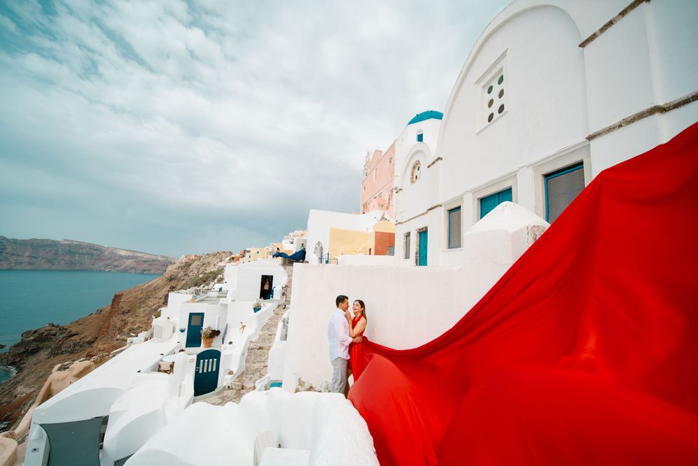 Flowing red dress contrasts against white buildings and blue domes of Santorini.