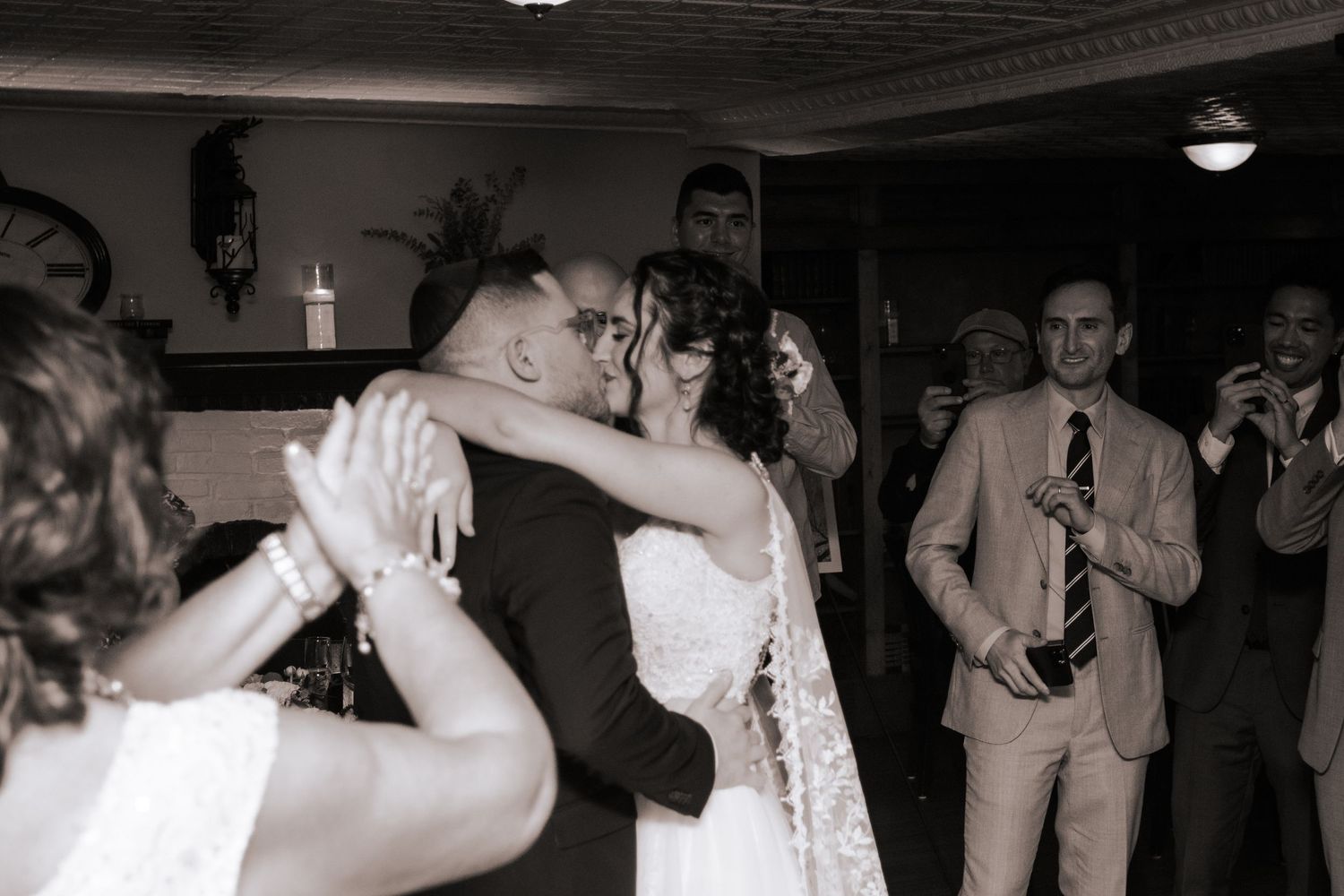 A newlywed couple kissing on the dance floor at their reception, surrounded by loved ones.
