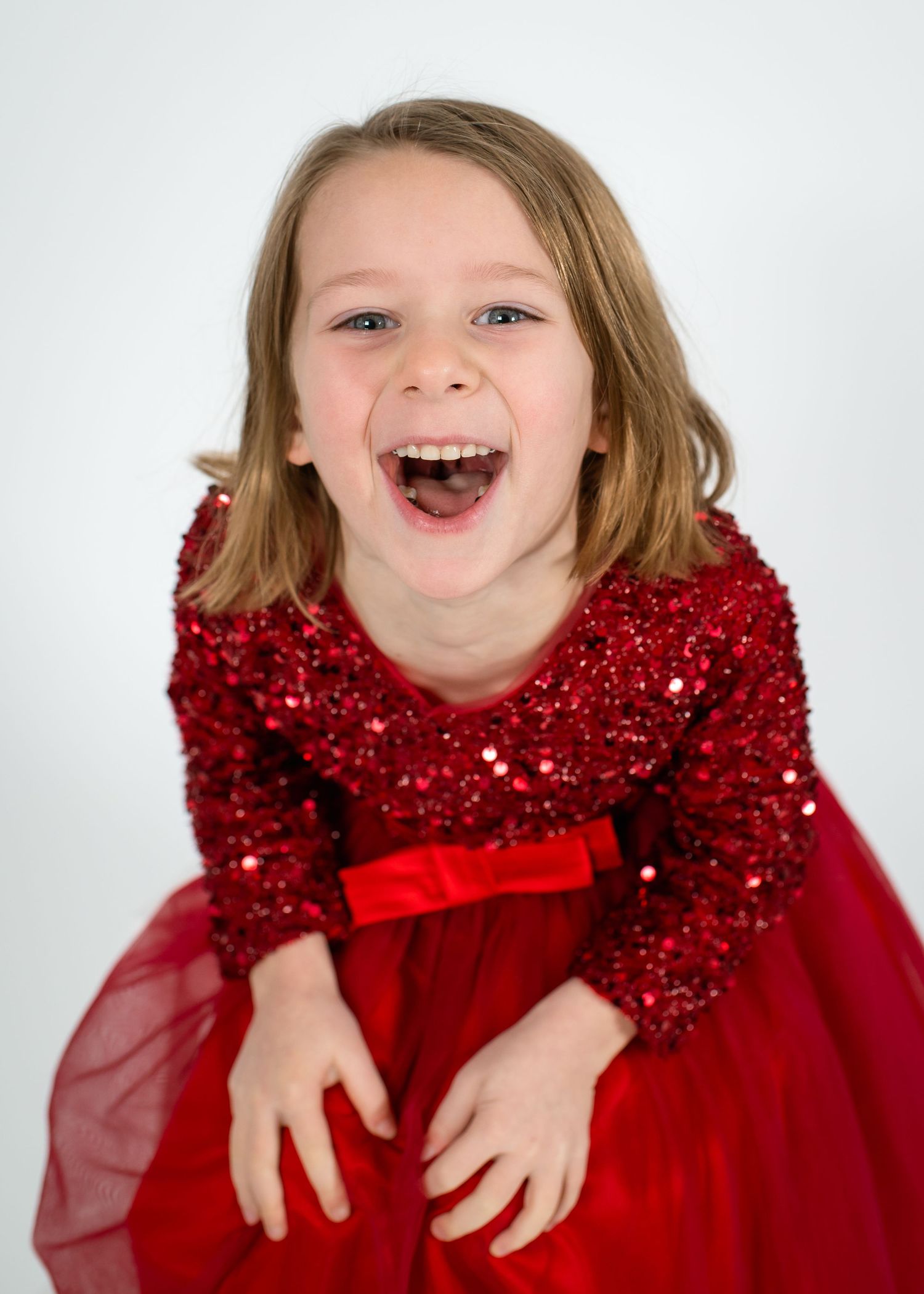 A child wearing a sparkly red holiday dress poses against a white background.