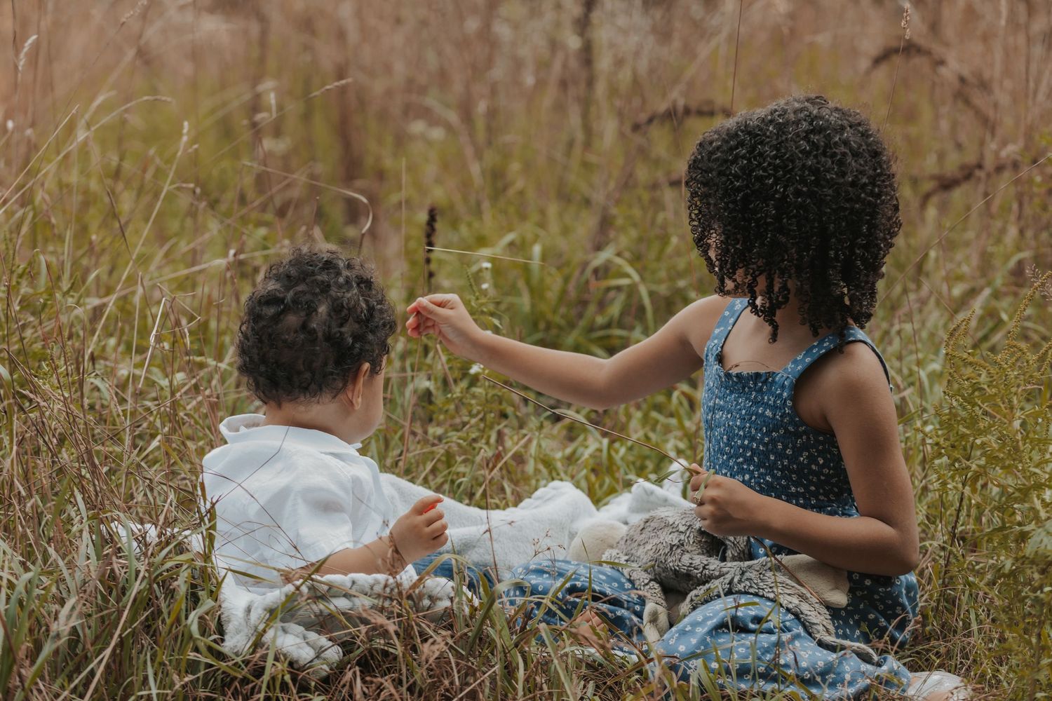 Siblings enjoying a picnic in a rustic outdoor field with tall grass and natural lighting in New England.