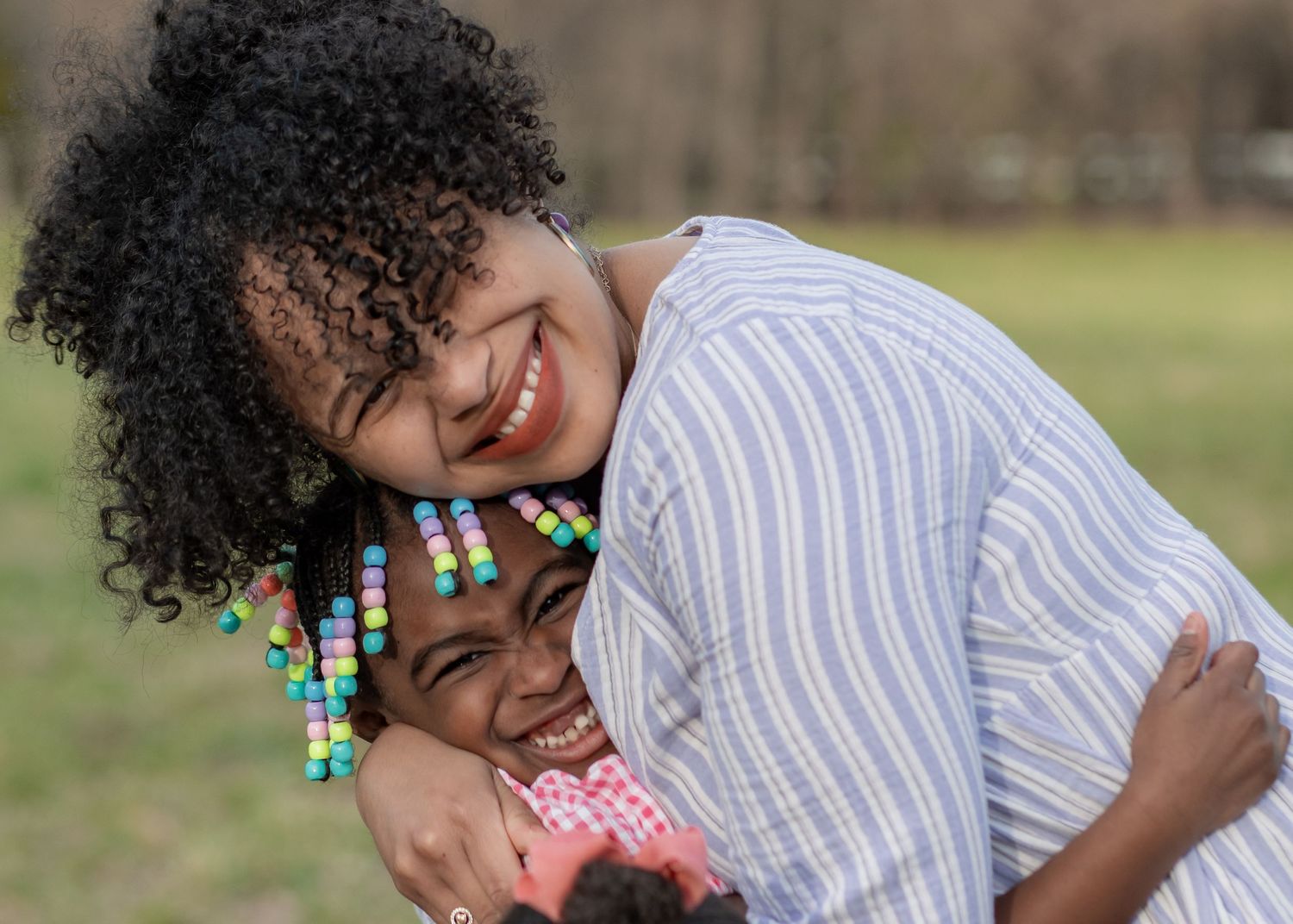 A candid photo showing a mother in a striped shirt and curly hair laughing joyfully outdoors while embracing her daughter in East Providence