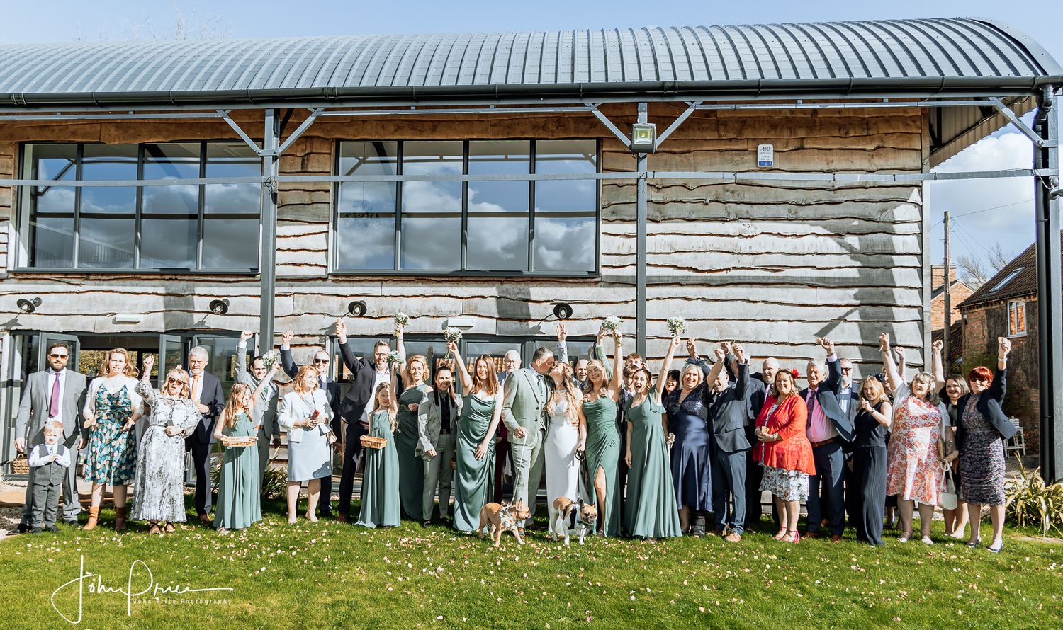 Wedding party and guests lined up for a group photo outside a rustic wooden building.