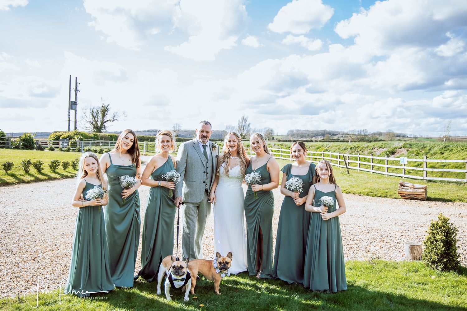 Wedding party in sage green dresses posing with a dog on a countryside path.