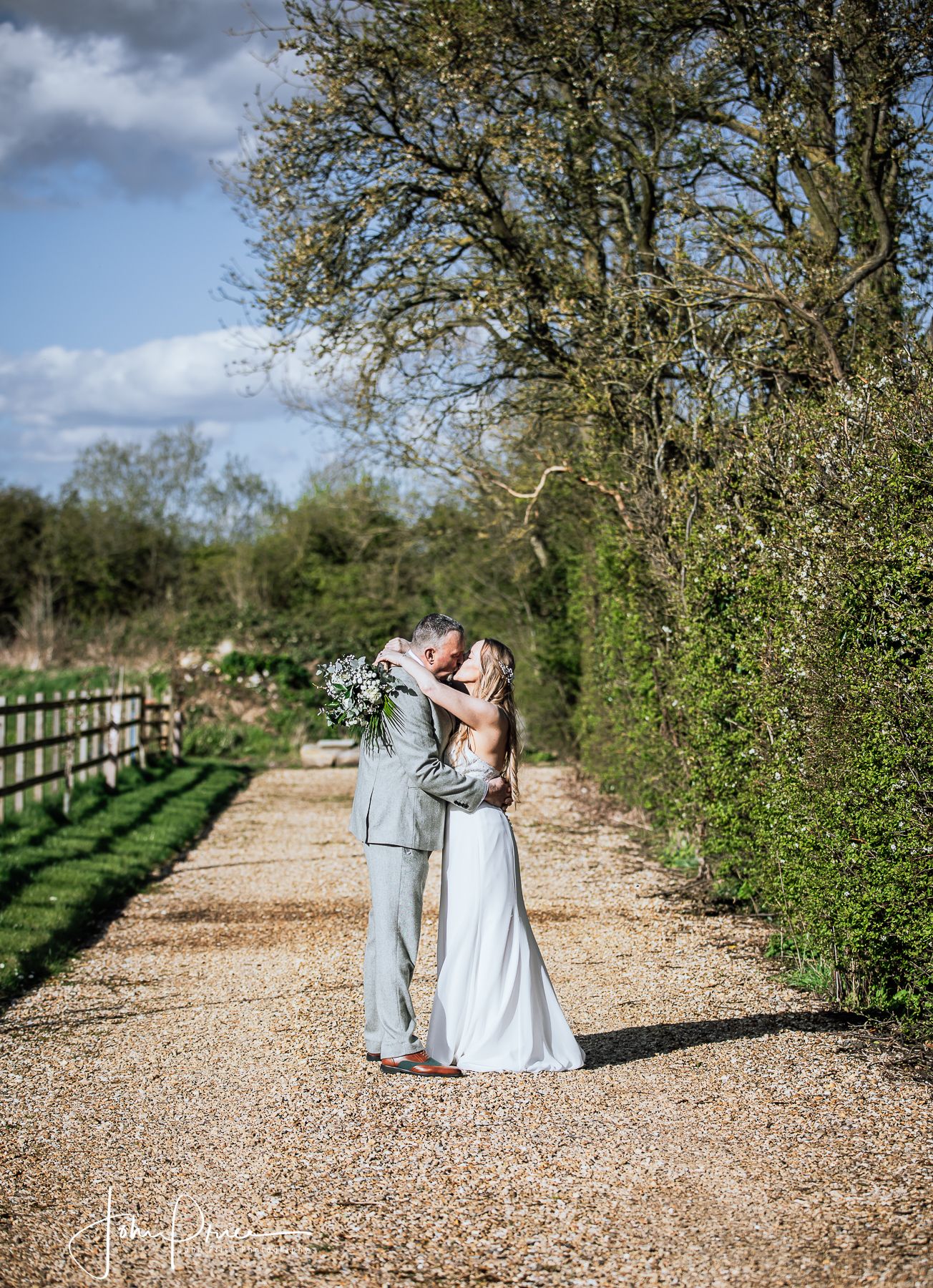 Romantic embrace on a countryside path with wooden fencing and hedges.