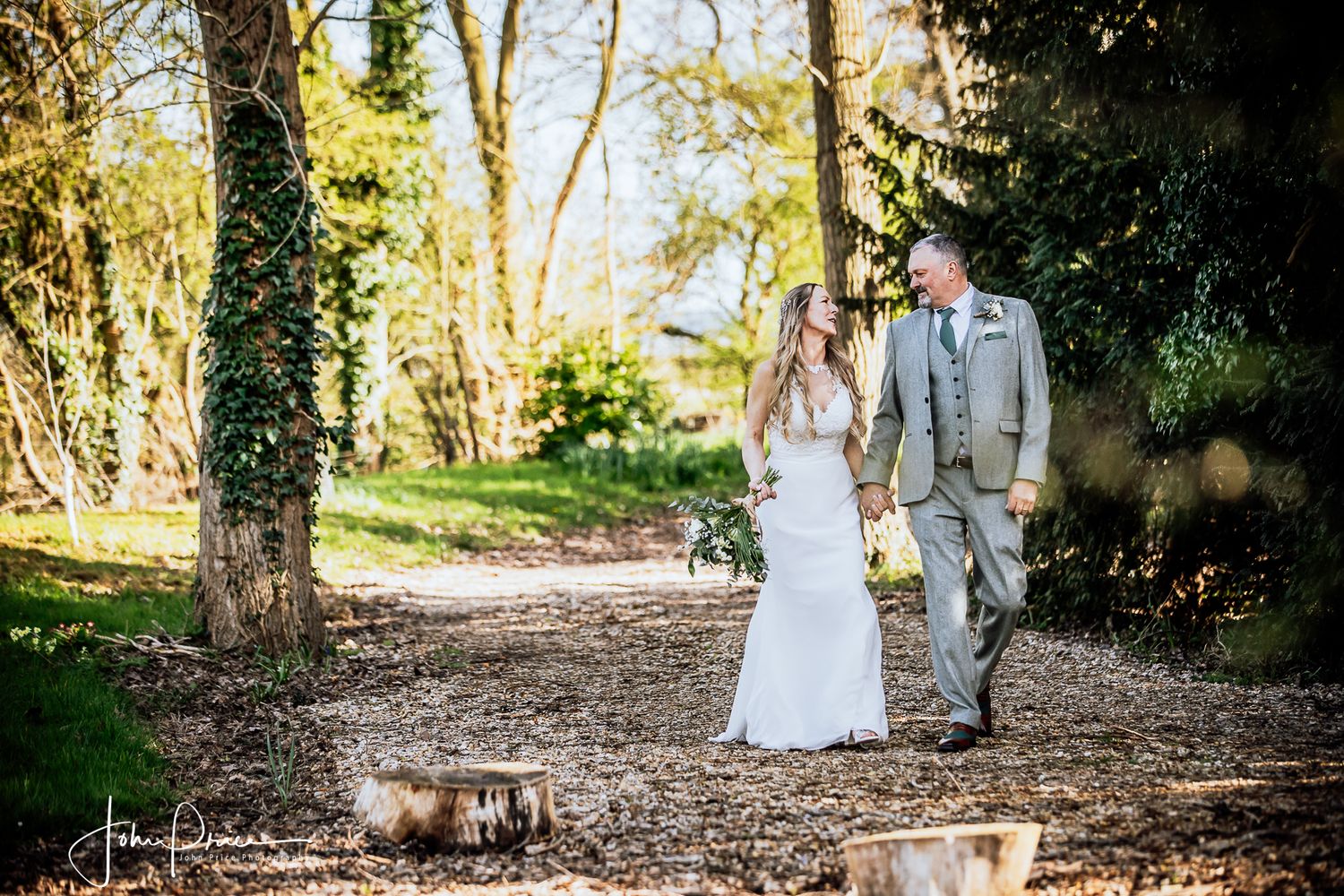 Couple walking along a tree-lined path in wedding attire.