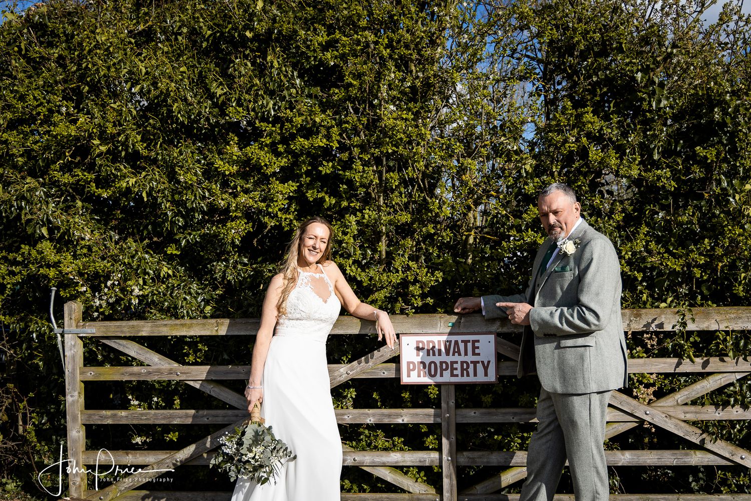 Couple posing by a wooden gate with a private property sign during their wedding photoshoot.