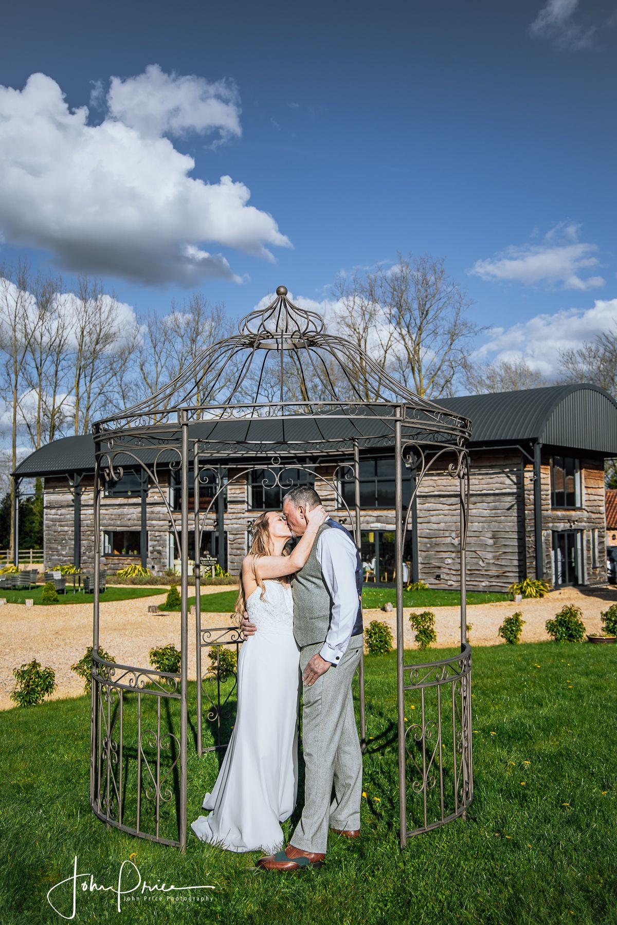 Wedding couple embracing in a garden gazebo with rustic venue in background.