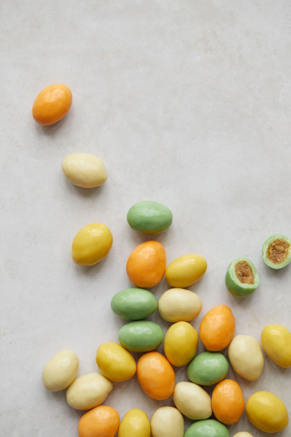 Colorful pastel candy-coated almonds scattered on light gray surface.