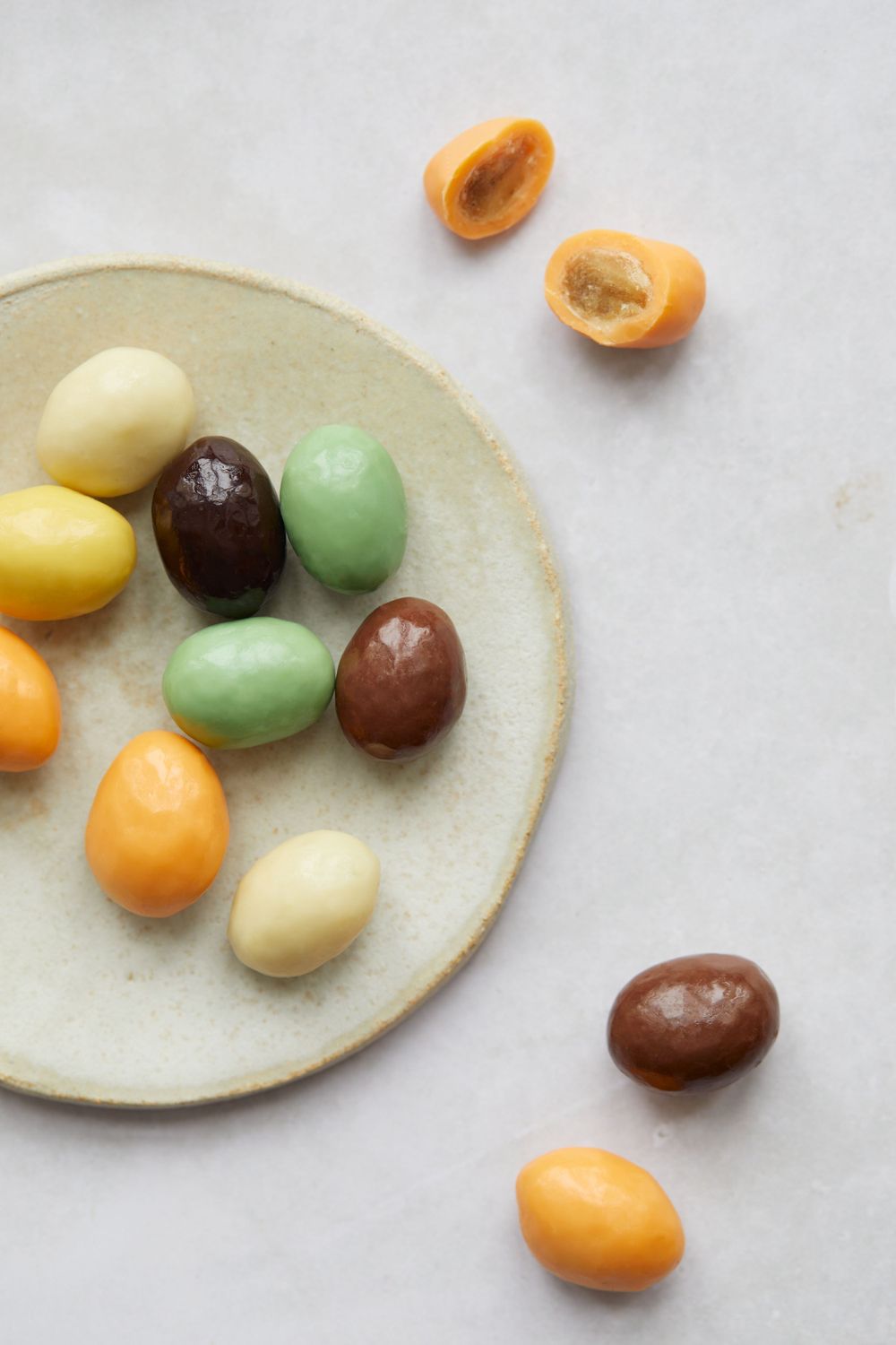 Assorted colorful candy-coated nuts arranged on a ceramic plate against white background.