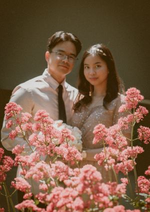 Romantic couple pose amid blooming pink flowers in a vintage-style portrait.