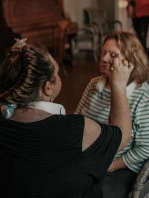 Behind-the-scenes makeup application in warm, moody lighting.