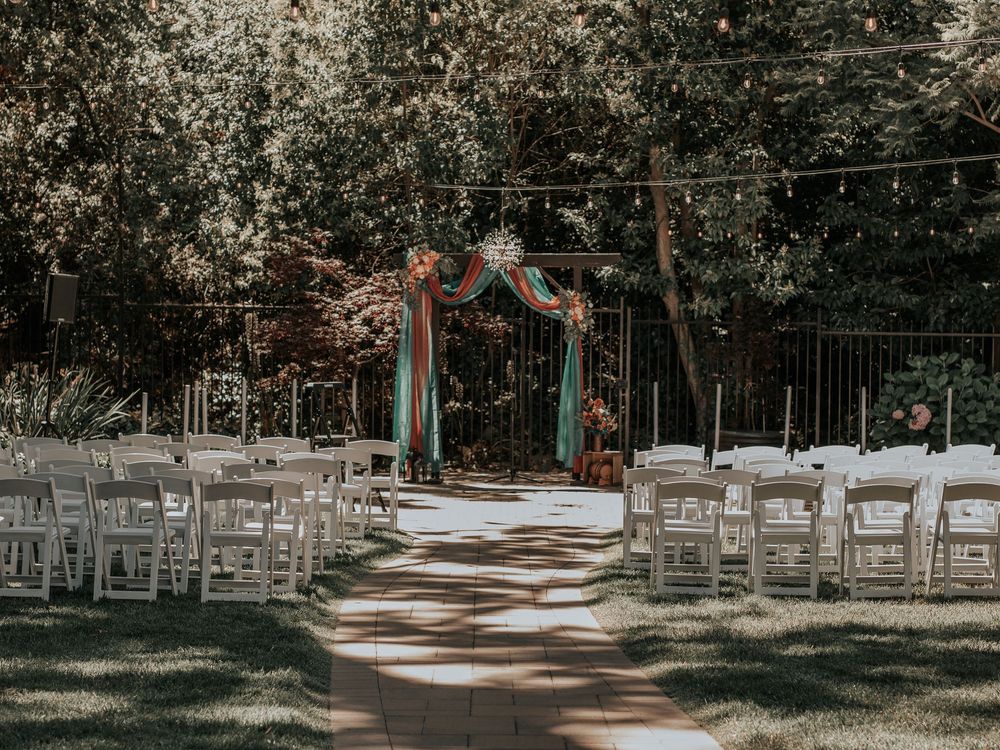 Outdoor wedding ceremony setup with white chairs and wooden arch among trees.