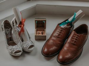 Wedding shoes including elegant white heels and brown leather oxfords arranged with a small wooden box.