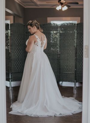 Elegant white wedding dress with lace details and flowing train shown from behind.