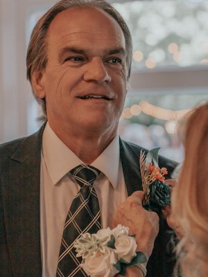 Wedding attendee wearing plaid tie and boutonniere smiling at outdoor reception.