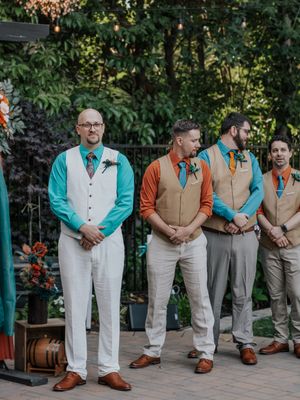 Wedding party members in coordinated turquoise and orange vests standing in garden setting.