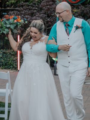 Joyful couple celebrating during outdoor wedding ceremony with greenery backdrop.