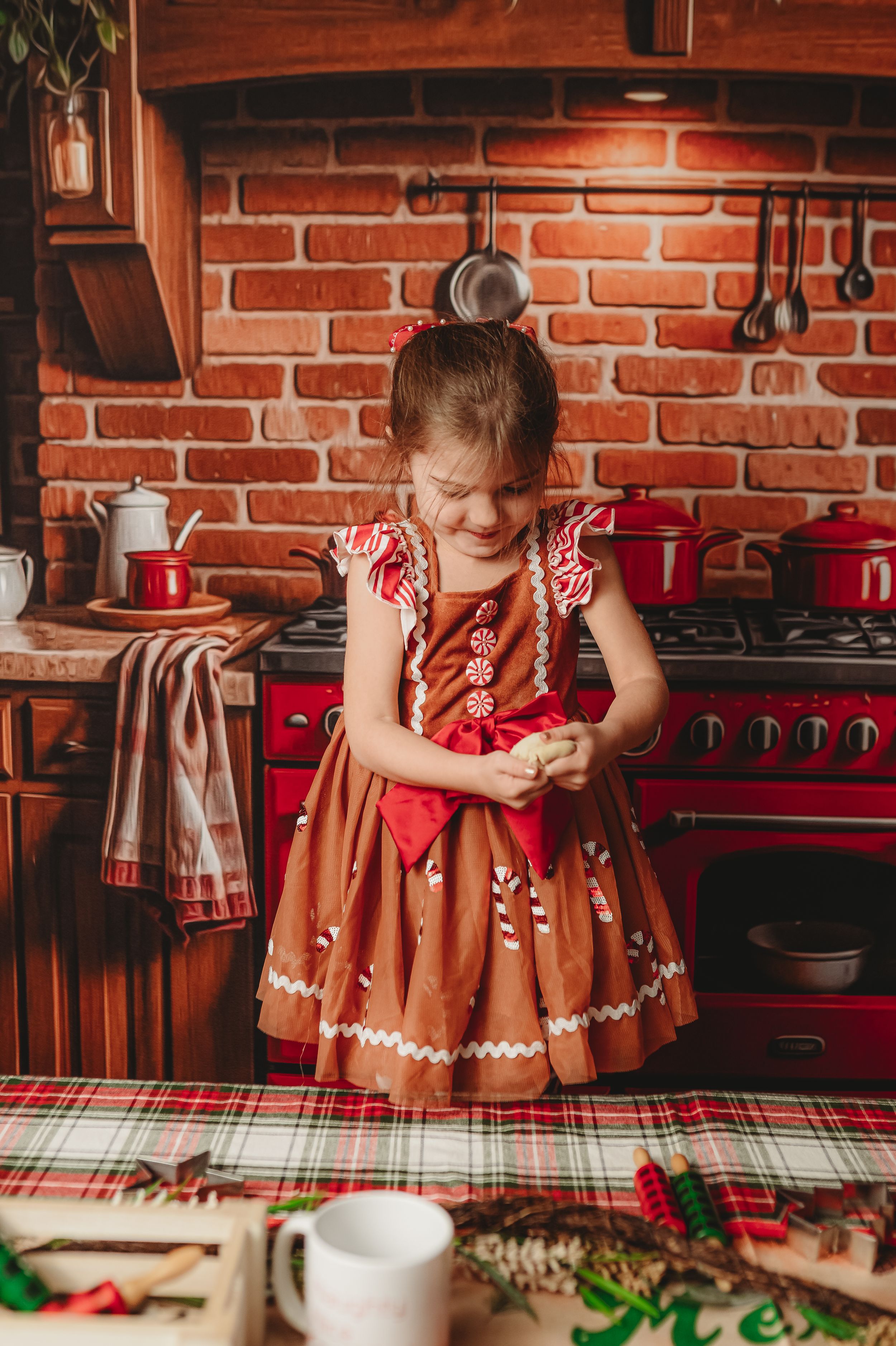 A festive holiday kitchen scene with a brown gingerbread dress and red vintage stove against exposed brick walls.