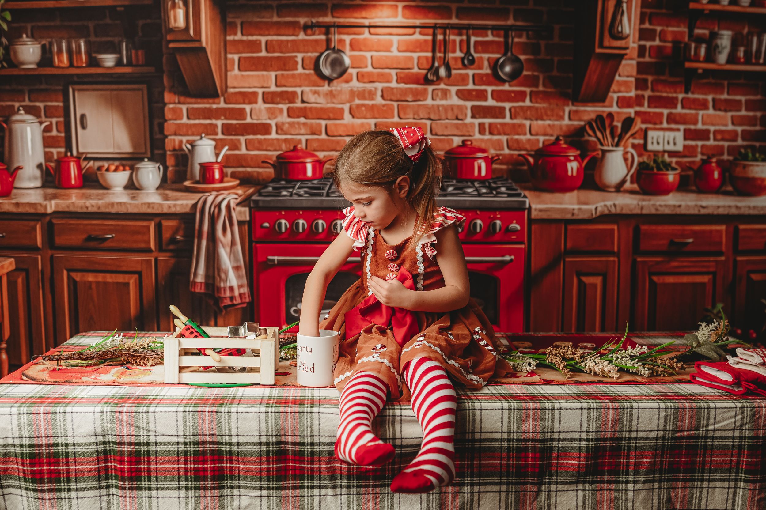 Cozy Christmas kitchen setting with plaid tablecloth and vintage red stove against brick backdrop.