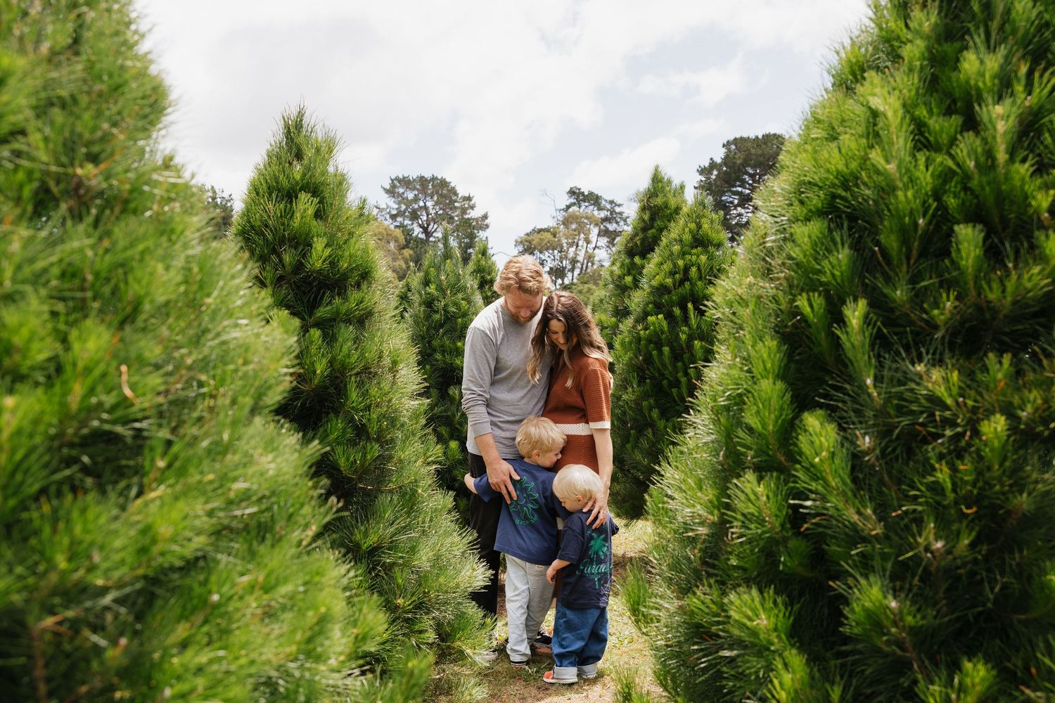 A joyful outdoor family moment among evergreen trees on a cloudy day.