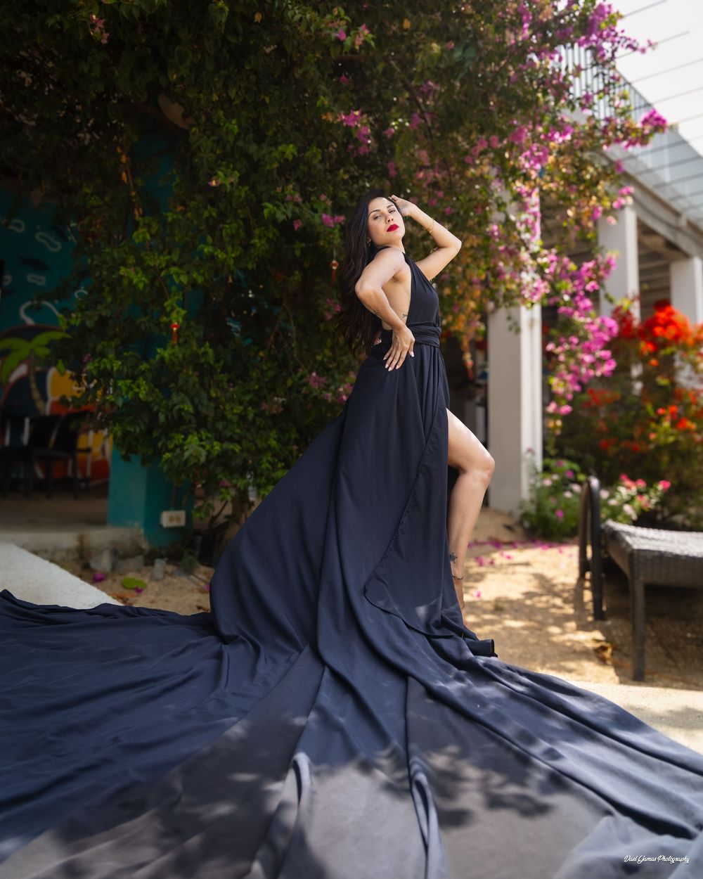 A flowing navy blue maxi dress billows elegantly in the breeze against a backdrop of pink bougainvillea flowers.
