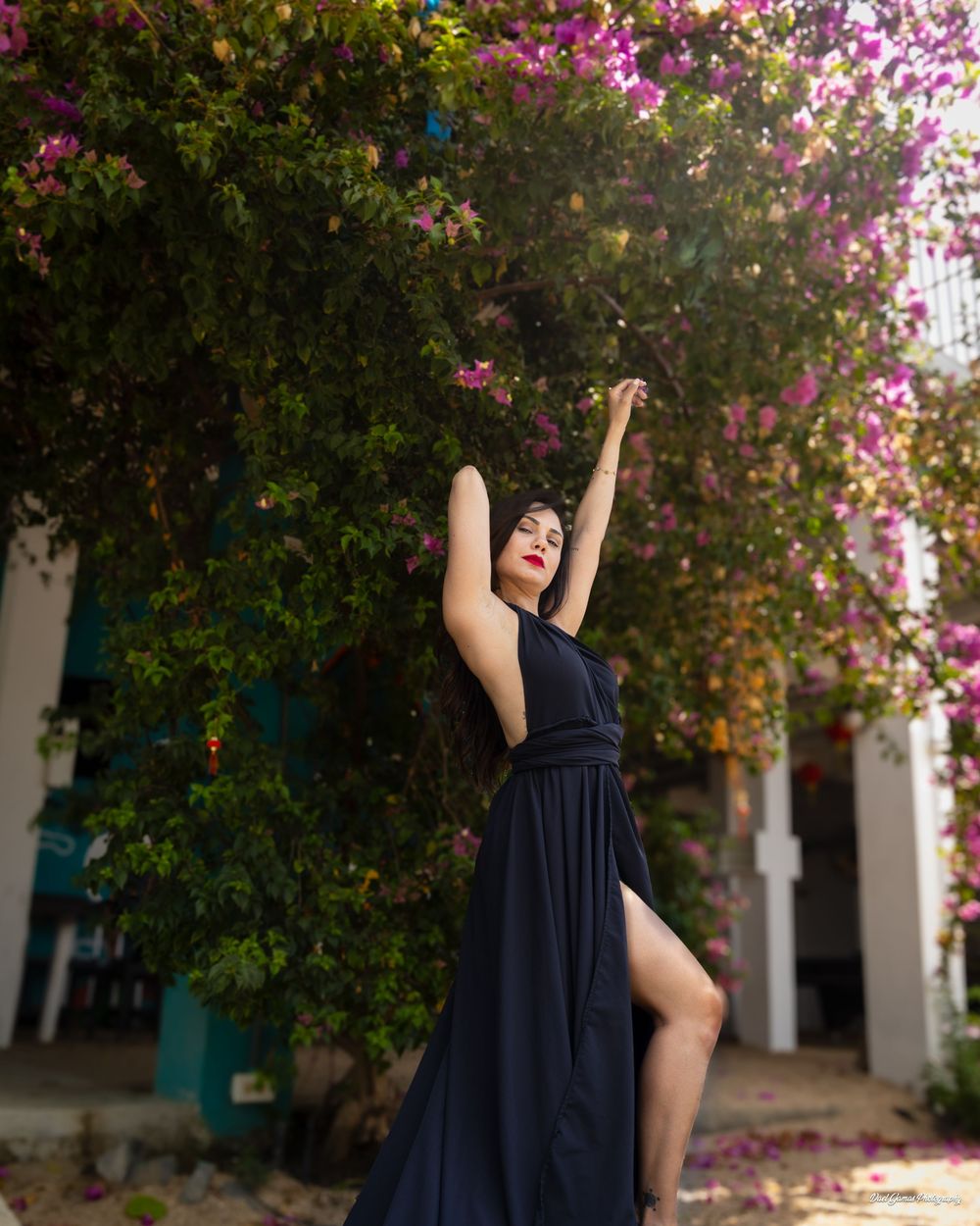 A graceful figure in a flowing navy dress poses elegantly against a backdrop of vibrant pink bougainvillea flowers.