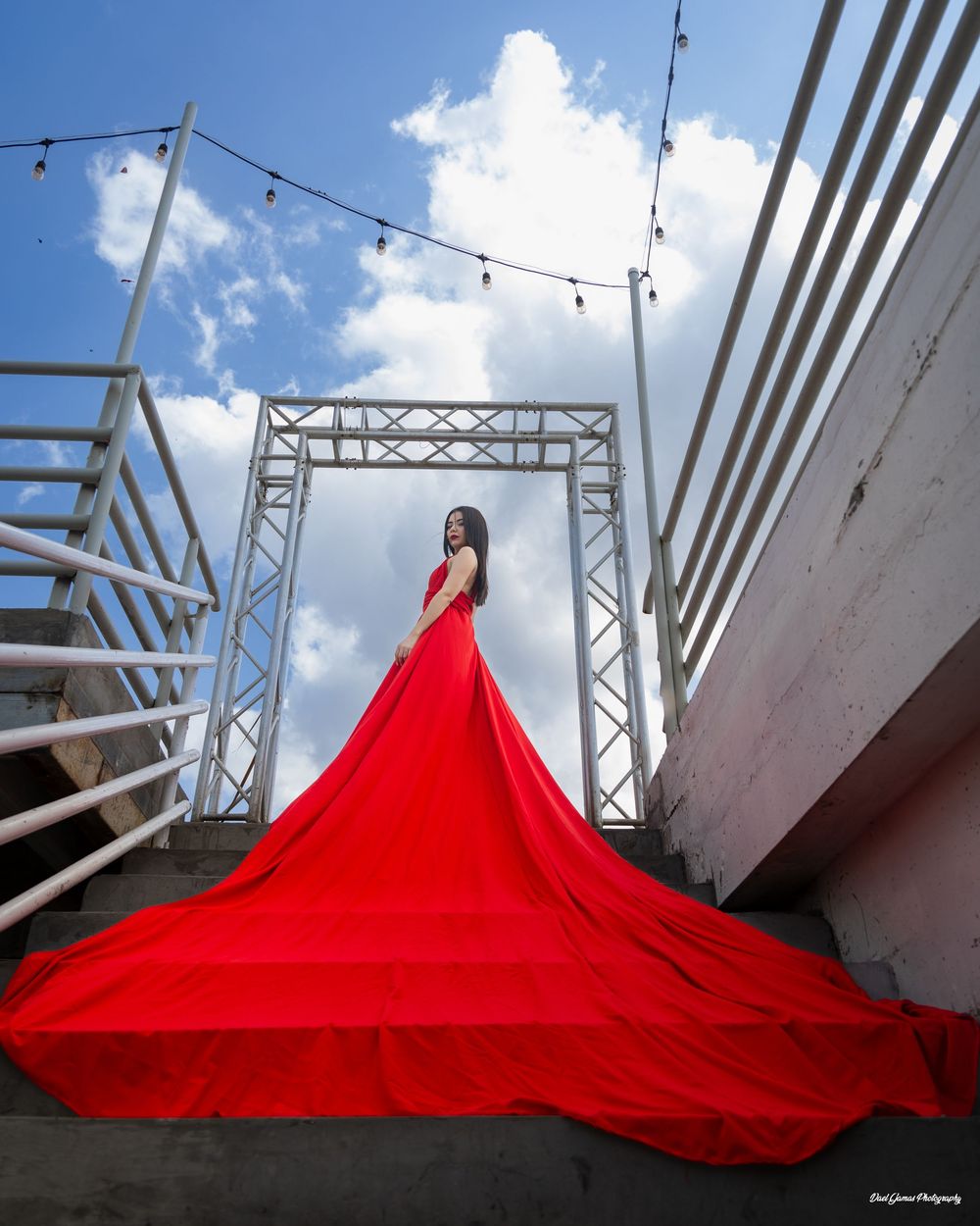 A flowing red fabric creates dramatic shapes against an industrial backdrop with metal beams and blue sky.