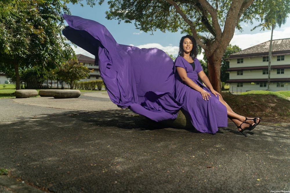 A person in a flowing purple dress performs a graceful spinning motion in a park setting.