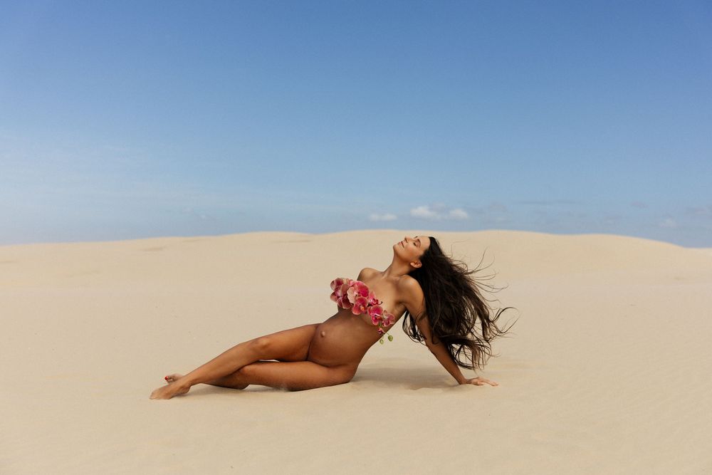 A person in a red bikini reclines on golden sand dunes under a bright blue desert sky.
