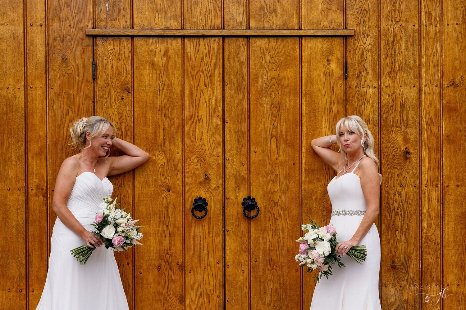 TWO brides posing against a rustic wooden wall background.