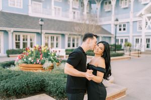 A couple embraces and laughs together during a romantic photoshoot in front of coastal beach houses.