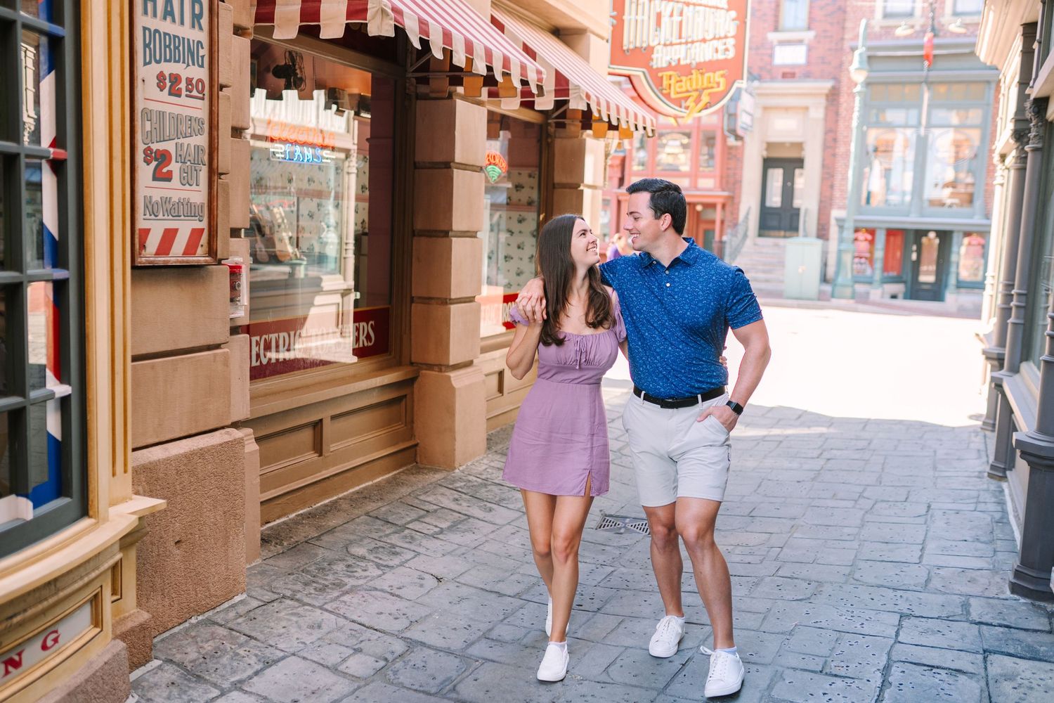 Couple walking hand-in-hand past charming storefronts with red awnings on a sunny day.