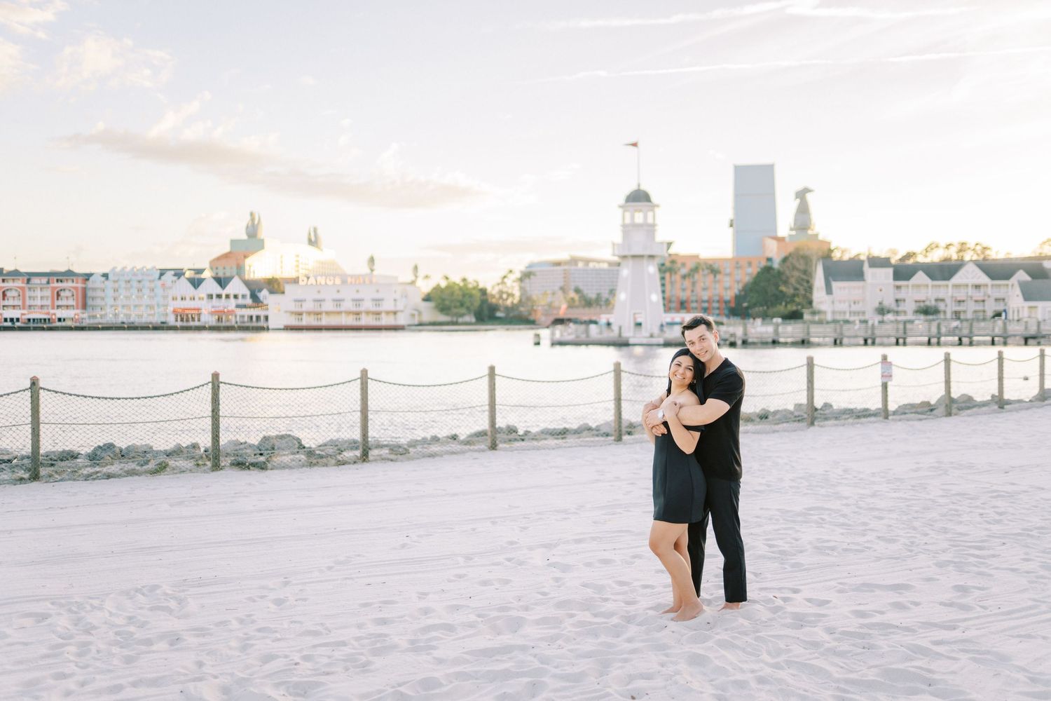 A couple shares an intimate moment on a wooden pier overlooking a waterfront cityscape.