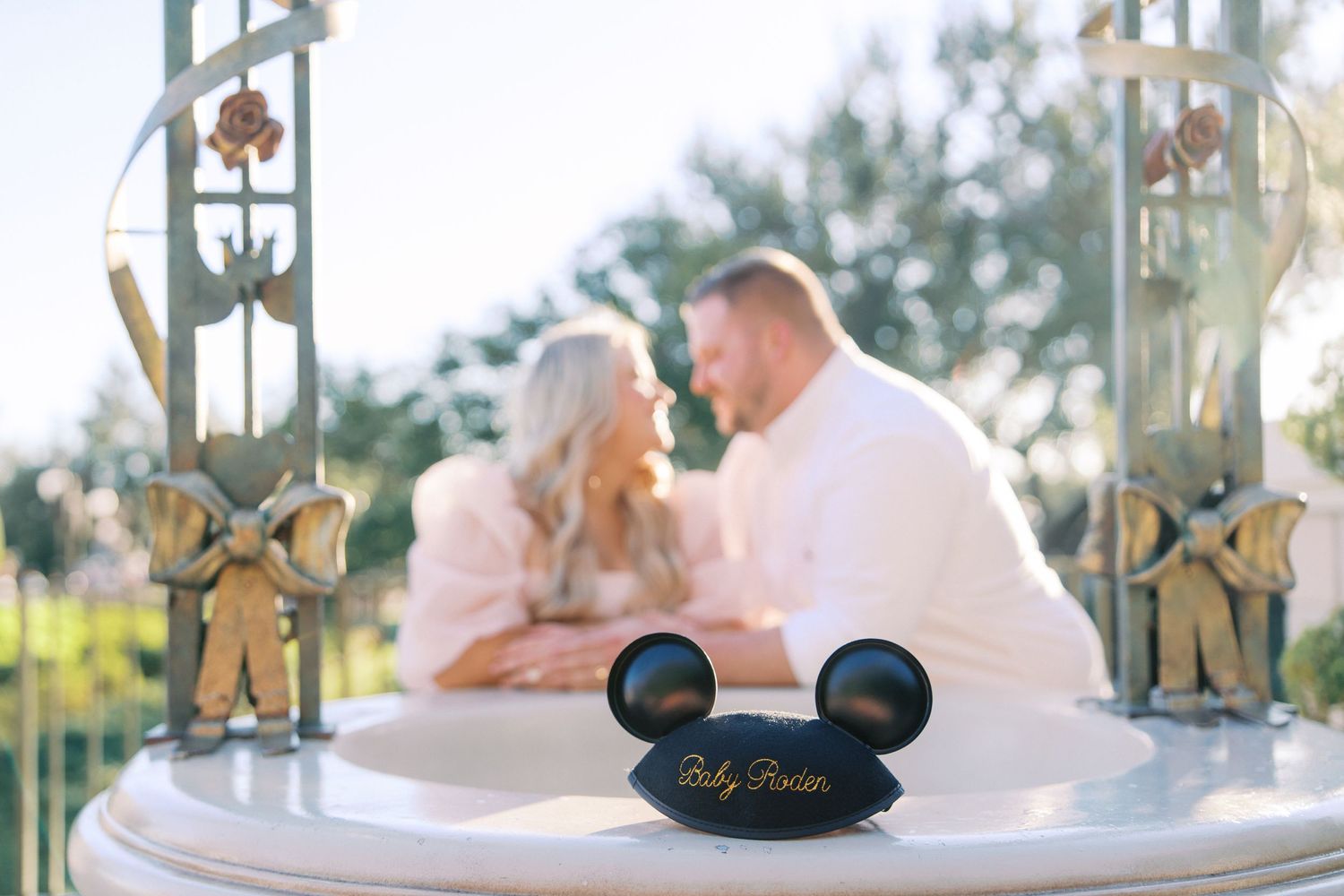 A Mickey Mouse ears keepsake sits on a white plate in the foreground of a romantic outdoor setting.